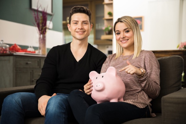 Couple sitting on couch with piggybank in hand.